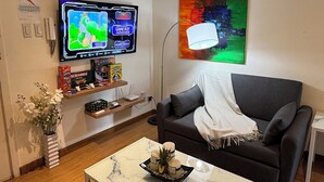 Ein Wohnzimmer mit Fernseher, einer Couch, einem Couchtisch und einem Bild an der Wand.