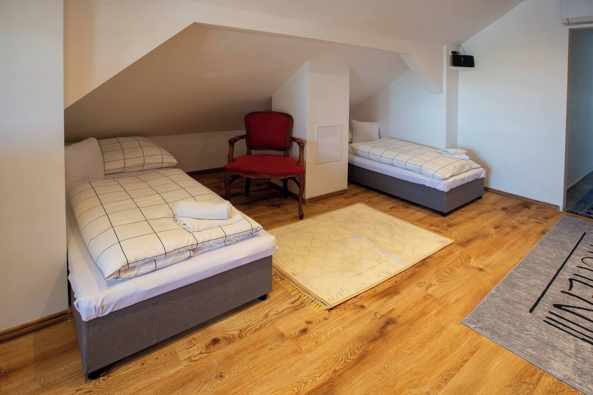 Een kleine, gezellige slaapkamer onder de pannen met twee bedden, een rode stoel en een houten vloer.