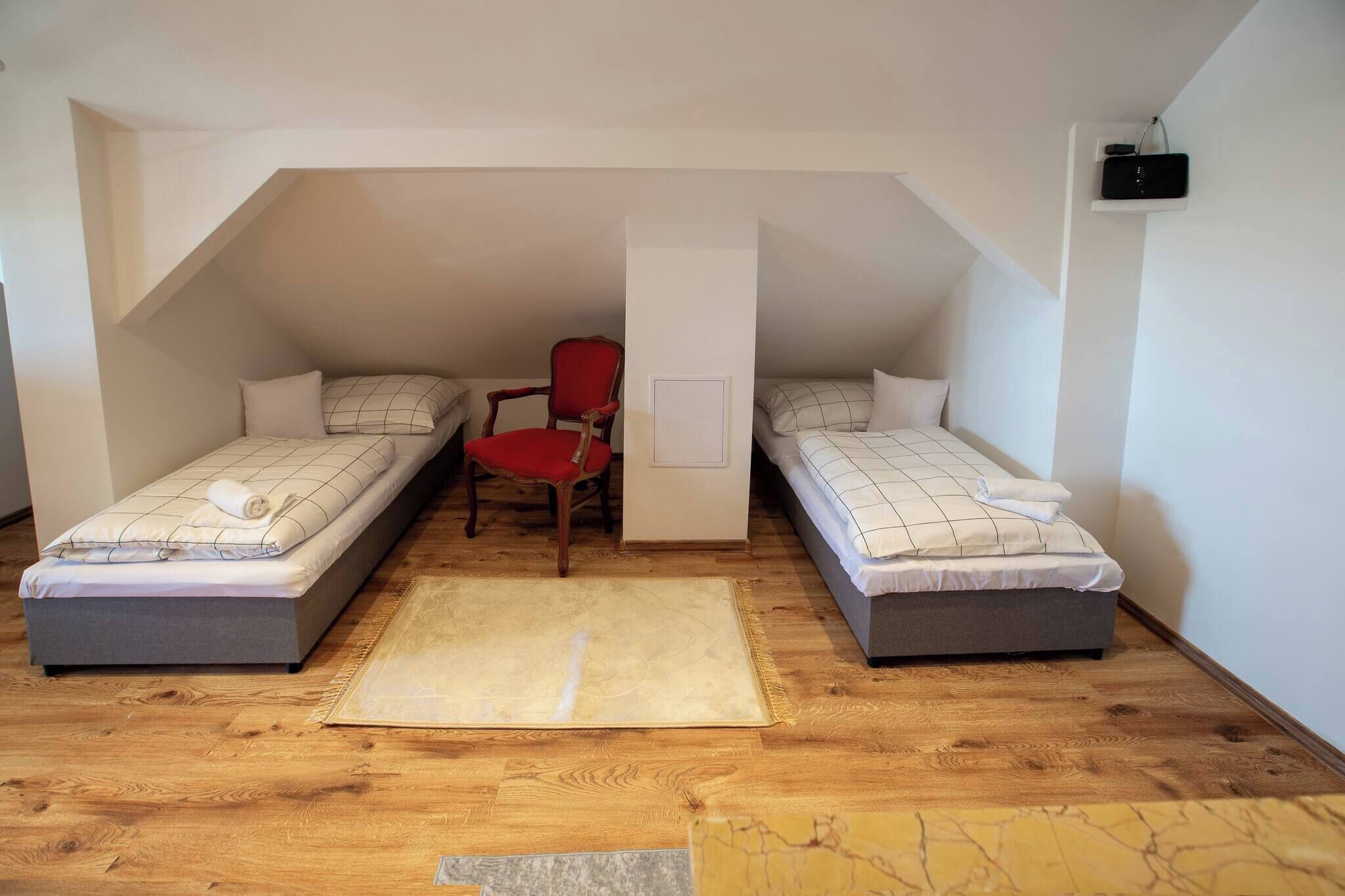A small, cozy attic bedroom with two single beds, a red chair, and a white wall-mounted radio.