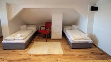 A small, cozy attic bedroom with two single beds, a red chair, and a white wall-mounted radio.