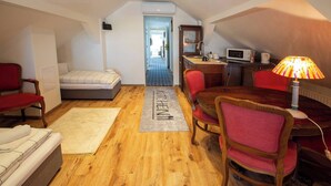 Ein kompakter, gut beleuchteter Raum mit einem Bett, einem Schreibtisch mit Computer, einem Sessel, einer Lampe und einer Mikrowelle. Ein Teppich mit dem Wort 'KITCHEN' ist sichtbar, was auf eine Küchenzeile hindeutet.