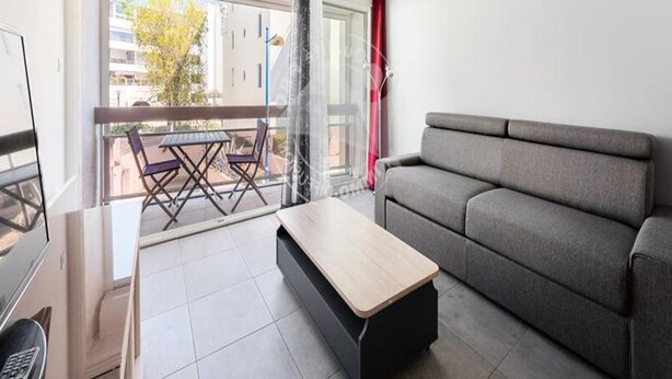 Un salon moderne avec un canapé gris, une table basse en bois et un balcon équipé d’une table et de chaises.