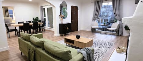 Uma sala de estar moderna com um sofá verde, uma mesa de centro de madeira e um espaço de jantar com um armário preto e cadeiras.