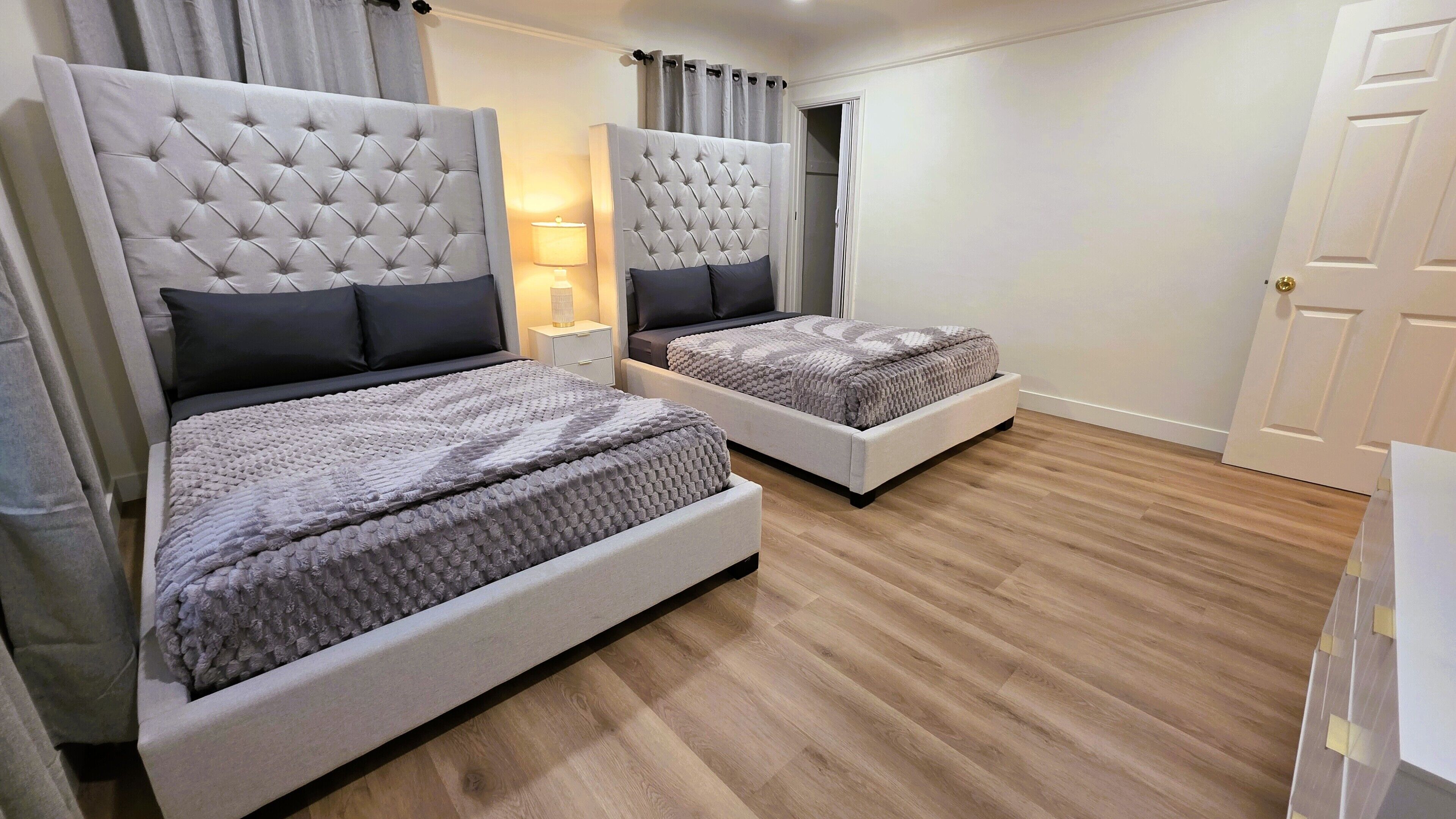 Een slaapkamer met twee bedden, een nachtkastje, een lamp en een deur.