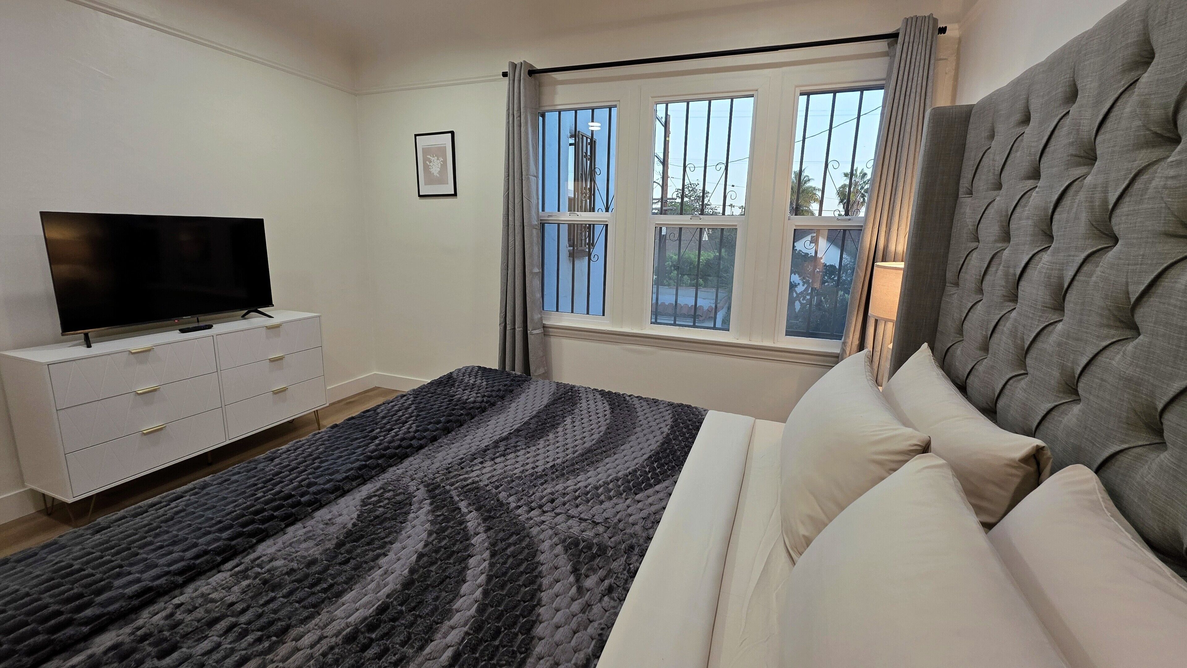 A bedroom with a bed, a TV on a dresser, and a window with bars.