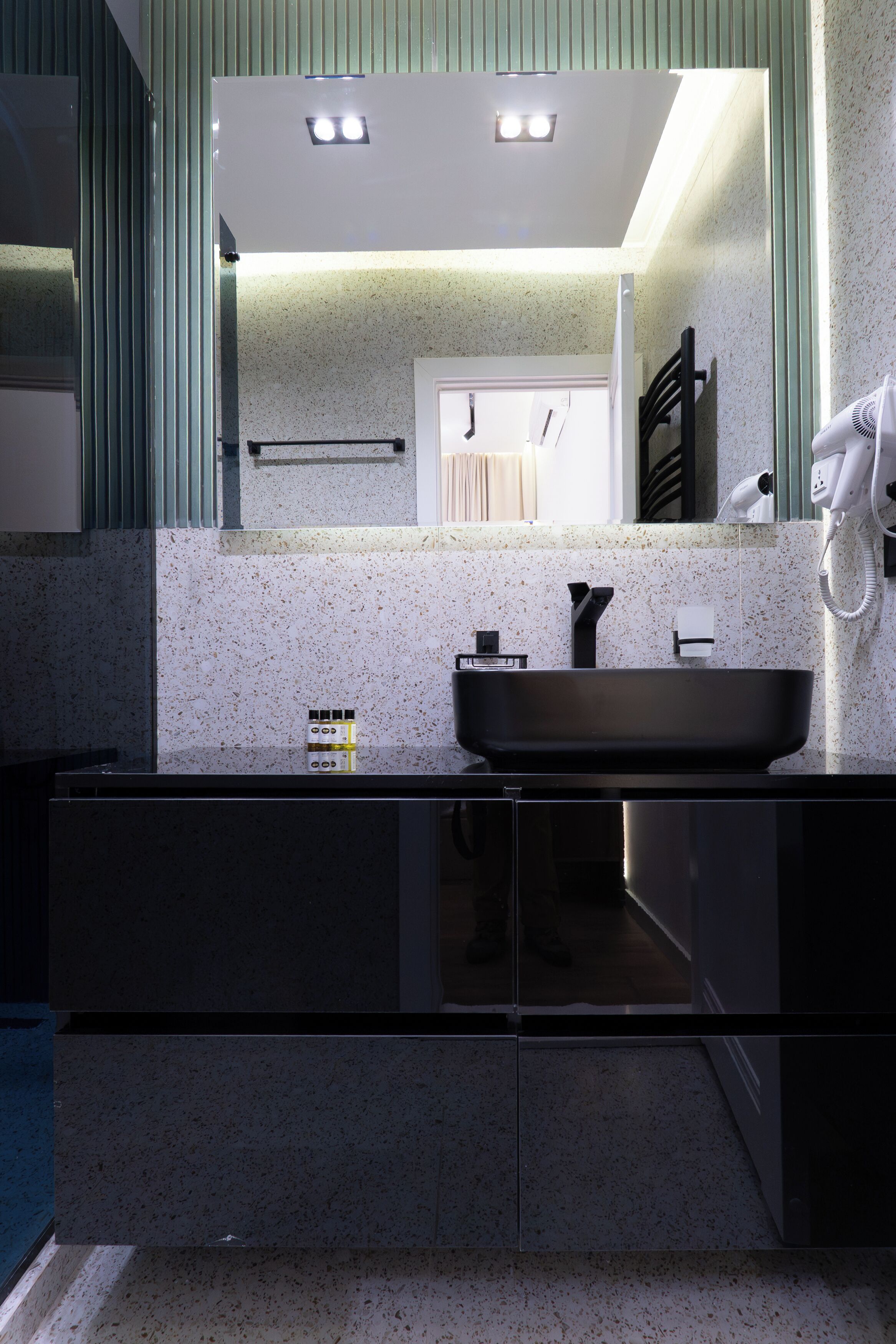Un bany modern amb un mirall gran, un lavabo negre i un suport per a tovalloles.