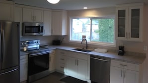 A modern kitchen with white cabinets, stainless steel appliances, and a window with a view of the backyard. - Charming Redmond 3-bedroom house with AC in a pleasant neighborhood- Sleeps 8 (Redmond)