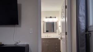 A hotel room with a flat-screen TV mounted on the wall, a dark-colored dresser, and a bathroom visible through an open door. - Charming Redmond 3-bedroom house with AC in a pleasant neighborhood- Sleeps 8 (Redmond)