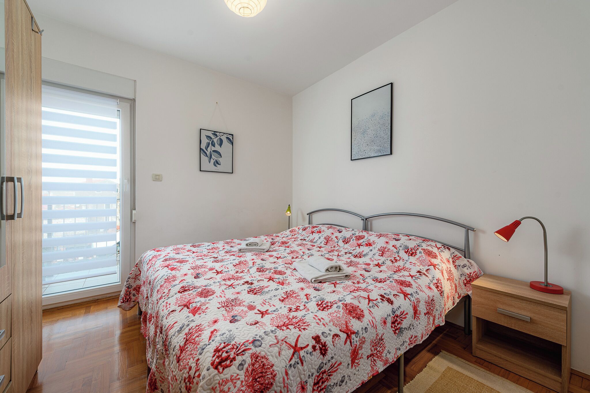 Un dormitorio con cama, mesita de noche, lámpara y ventana con persianas.
