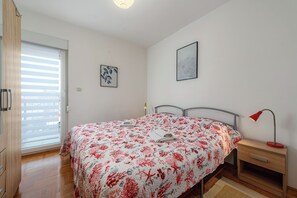 A bedroom with a bed, a nightstand, a lamp, a window with blinds, and two wall art pieces. - Ares 14 - Modern apartment with sea view, quiet location and close to the beach 20 m. (Umag)