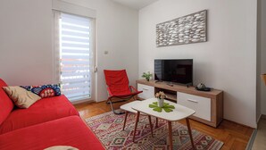 A living room with a red sofa, a small white table, a red chair, a TV on a wooden cabinet, and a patterned rug. - Ares 14 - Modern apartment with sea view, quiet location and close to the beach 20 m. (Umag)