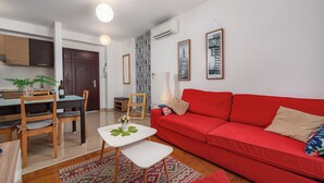 A living room with a red sofa, a small white table, and a dining area with wooden chairs. - Ares 14 - Modern apartment with sea view, quiet location and close to the beach 20 m. (Umag)