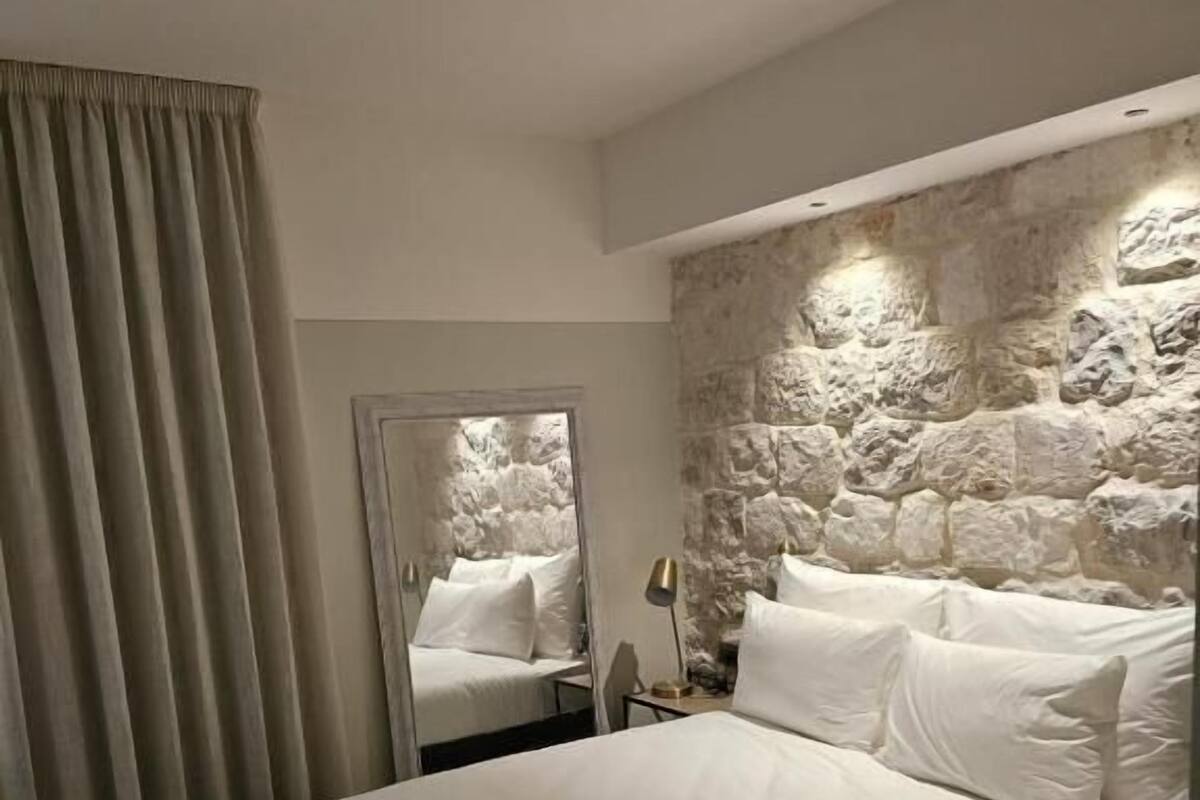 Un dormitorio con una cama grande, una pared de piedra, un espejo y una ventana con cortinas.