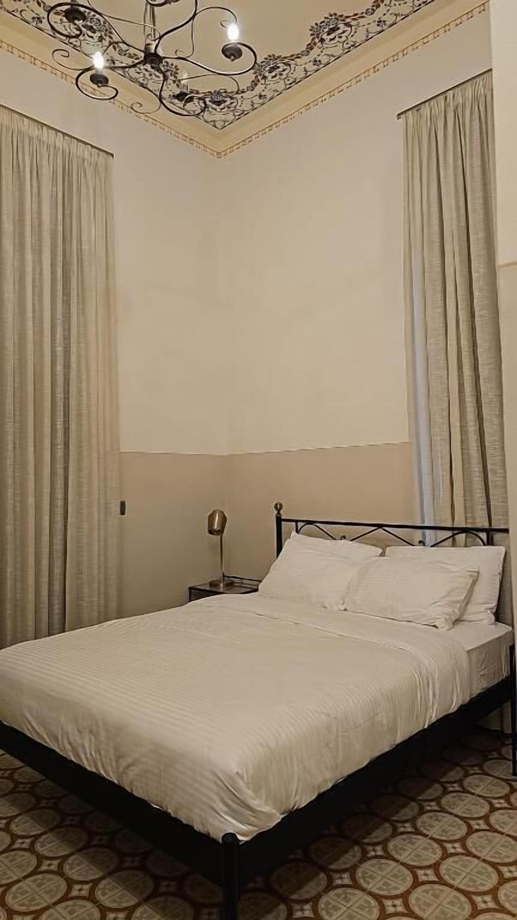 Quarto com cama, cortinas, um candelabro e piso estampado.