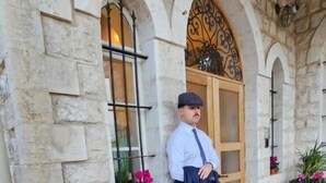 Ένας άνδρας στέκεται μπροστά σε ένα πέτρινο κτίριο με τοξωτά παράθυρα και μια ξύλινη πόρτα.