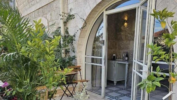 Μια αυλή με φυτά σε γλάστρες και ένα πέτρινο κτίριο με μια αψιδωτή είσοδο.