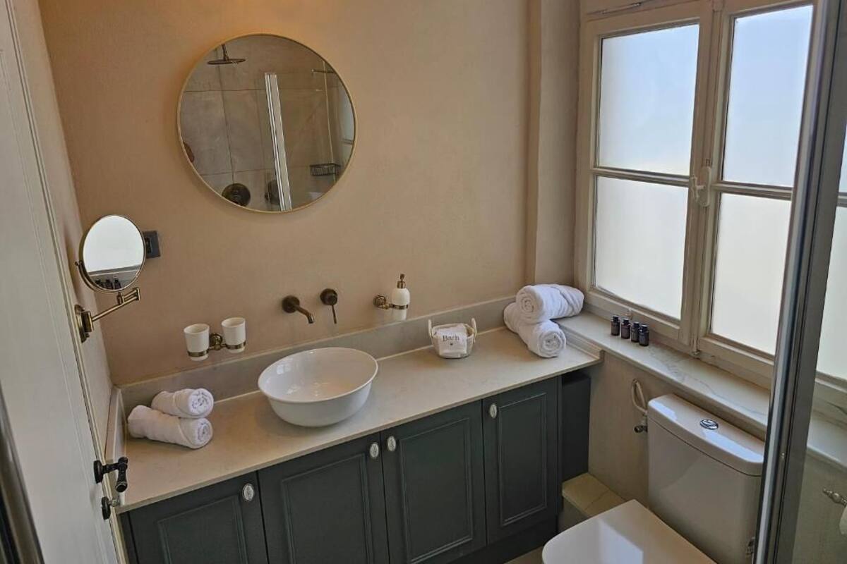 Un baño con un espejo redondo, un lavamanos amplio y una ventana.