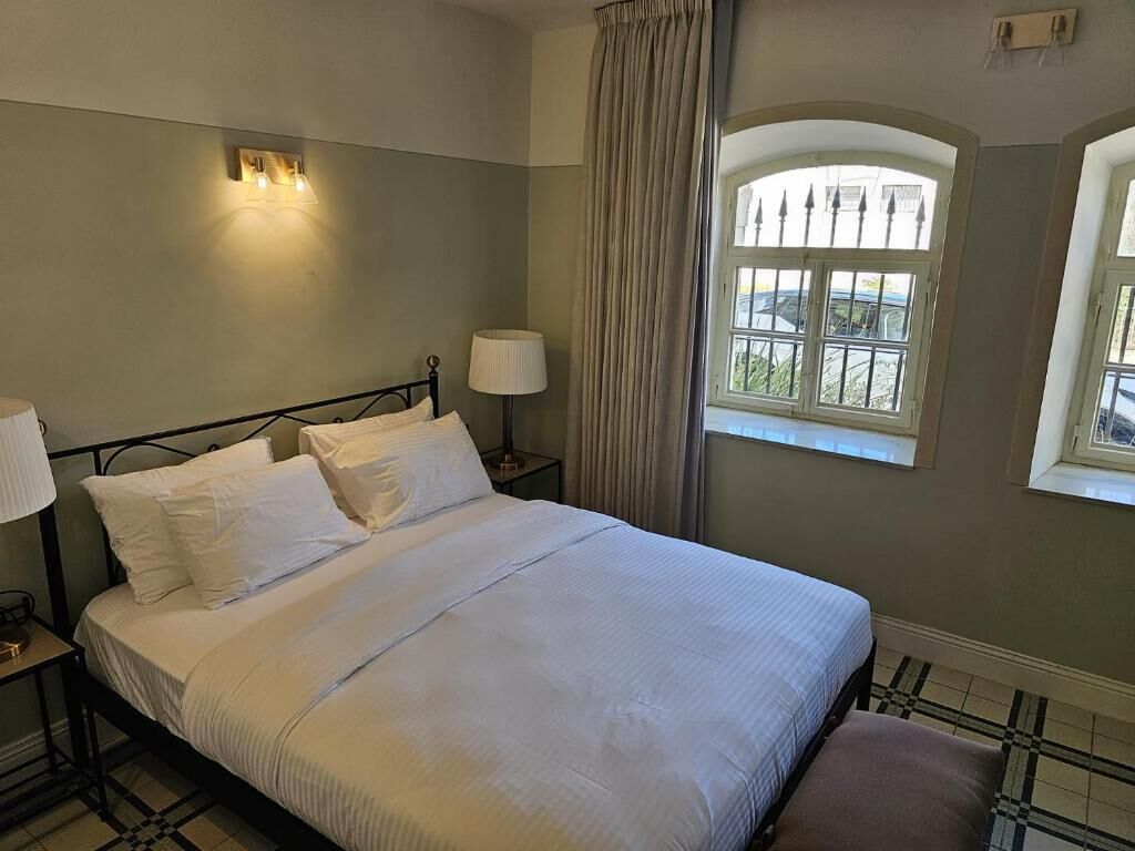 A neatly made bed with white linens, a bedside lamp, and a window with curtains.