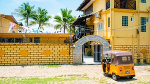 A yellow building with a brick wall, a gate, and a parked yellow auto-rickshaw. - Triple superior room, 2nd floor, Hôtel de charme avec Piscine, Nosy be (Nosy Be)