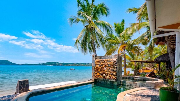 A clear infinity pool with a stone wall and palm trees, overlooking a calm sea and a distant island. - Triple superior room, 2nd floor, Hôtel de charme avec Piscine, Nosy be (Nosy Be)