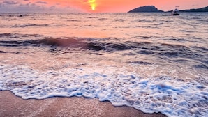 A beach with waves gently lapping onto the shore, a sunset in the background, and a small boat in the distance. - Triple superior room, 2nd floor, Hôtel de charme avec Piscine, Nosy be (Nosy Be)