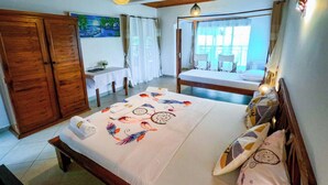 A bedroom with a large bed, a wooden wardrobe, a desk with a chair, and a view of the balcony. - Triple superior room, 2nd floor, Hôtel de charme avec Piscine, Nosy be (Nosy Be)