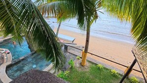 Zwembadterras met uitzicht op het strand, palmbomen en een ligstoel.