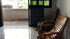 Una habitación con piso de baldosas, una silla de madera, una ventana que ofrece vistas a la vegetación y una puerta que da al exterior.