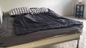 Una cama individual con un cojín de cuadros y una manta estampada en una habitación con suelo de baldosas y una ventana.