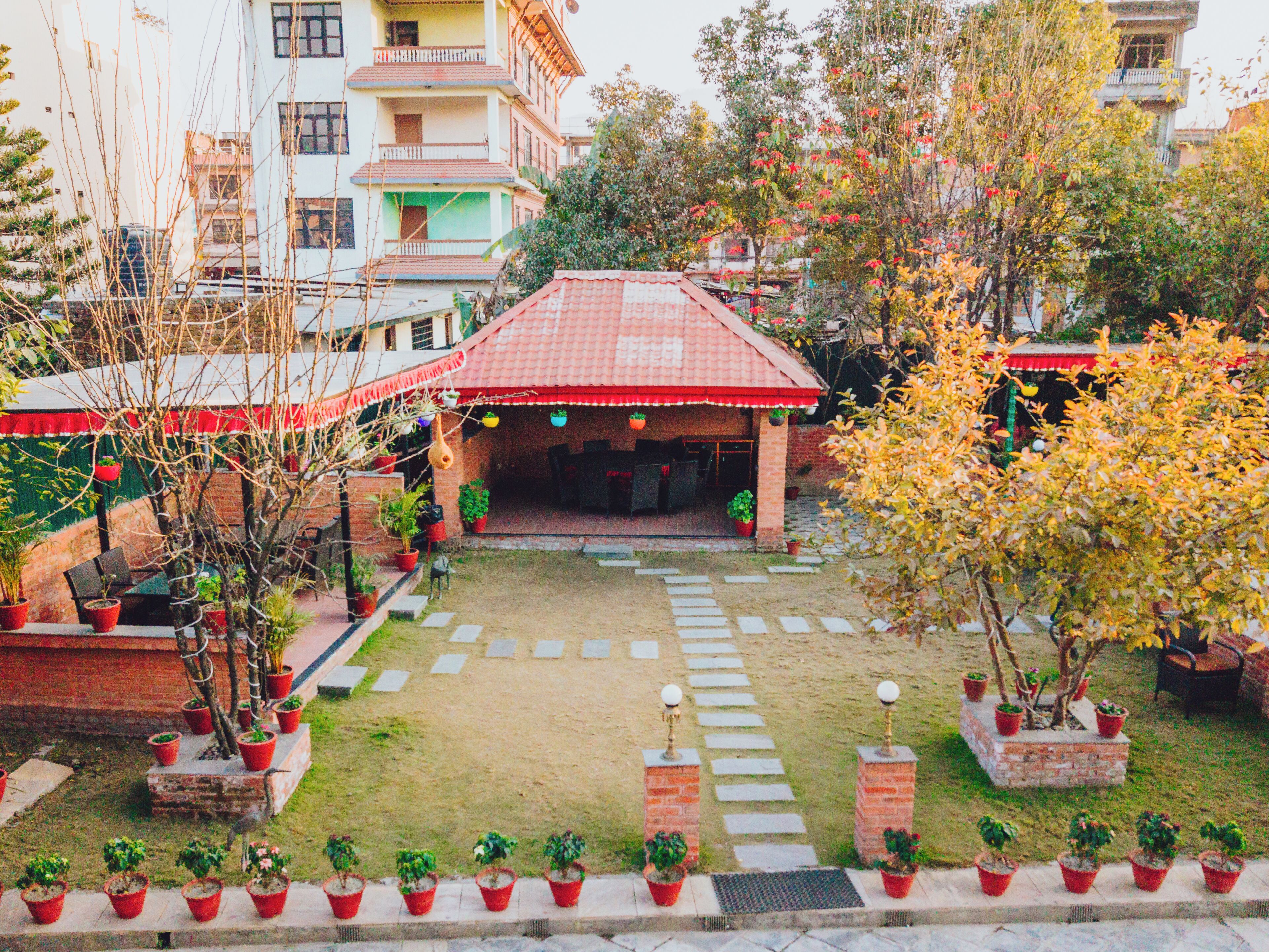Un patio con un edificio de techo rojo, plantas en macetas y un sendero pavimentado.