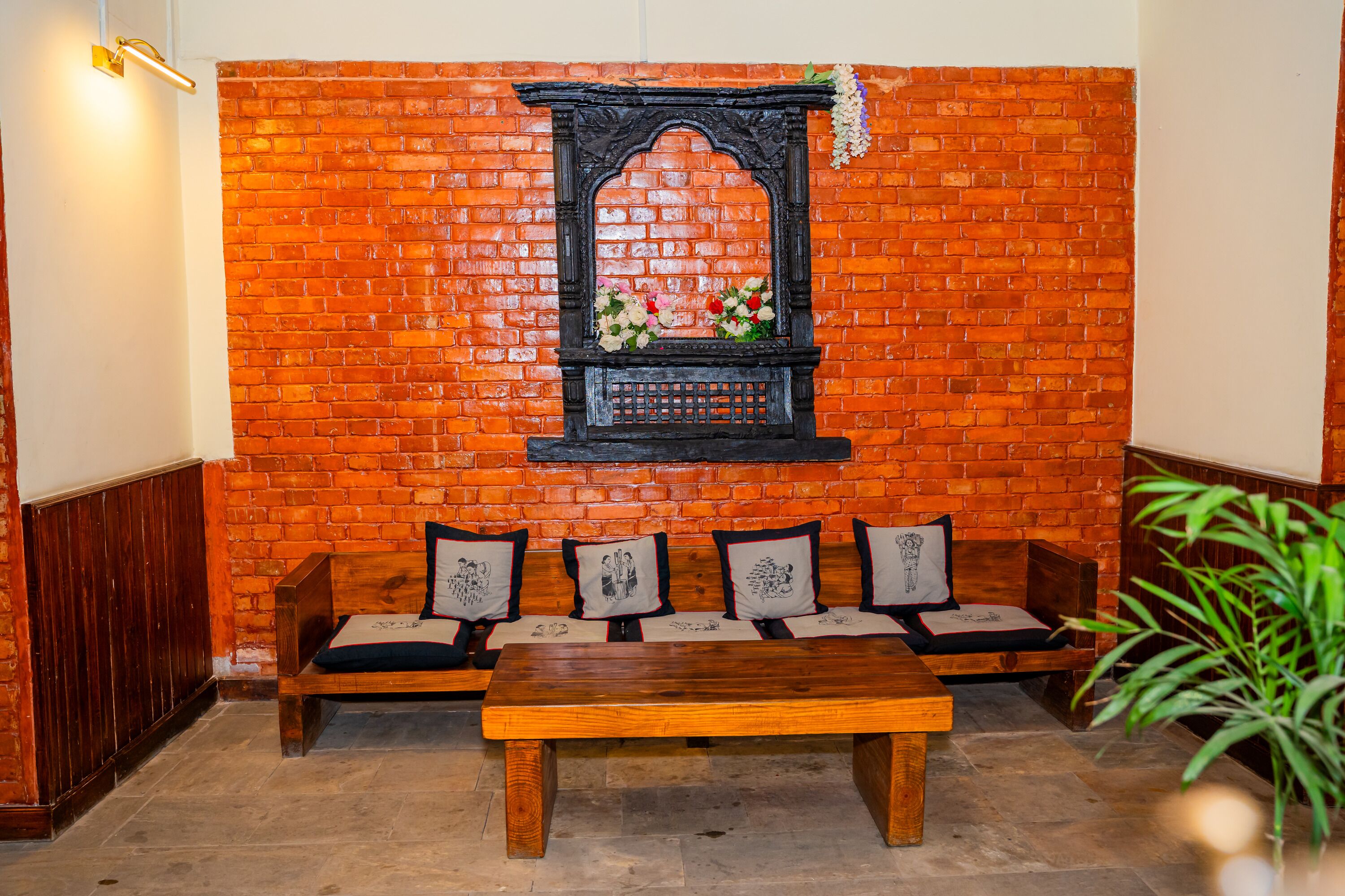 Una habitación con pared de ladrillo, un banco de madera con cojines, una mesa de madera y un arreglo floral colgante.