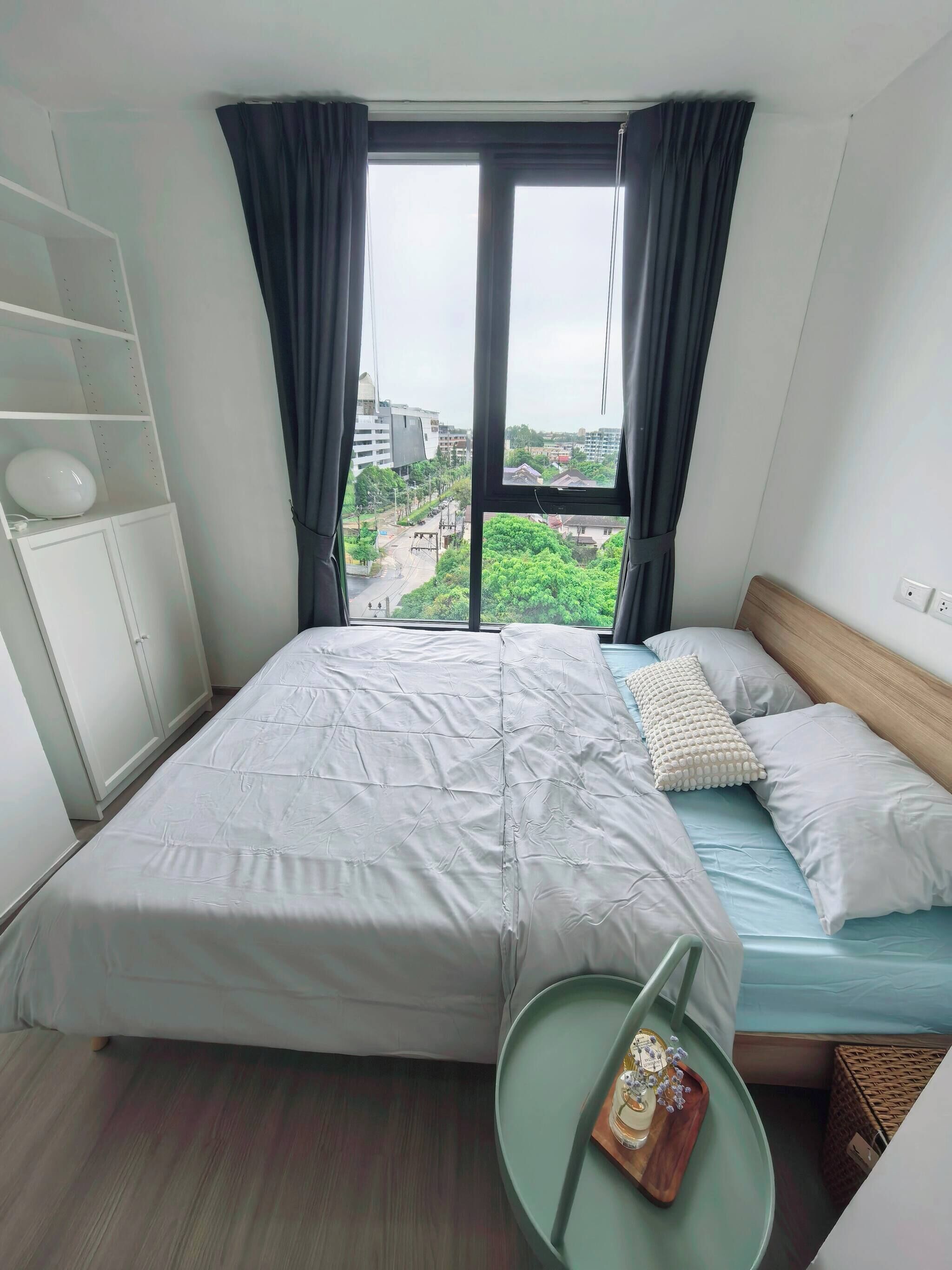 Habitación de hotel con cama, una mesita redonda con bandeja y vistas a la ciudad a través de amplias ventanas.