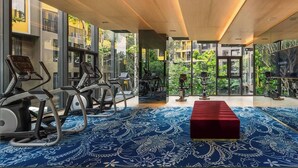 A gym with exercise equipment, a patterned carpet, and large windows offering a view of greenery. - Friendly 2BR in Phuket Central With Pool & gym (Wichit)