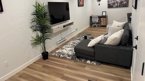 Een moderne woonkamer met een flatscreen televisie, een grijze bank, een plant in pot en kunstwerken aan de wanden.