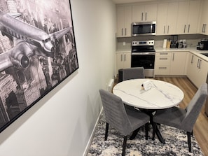 Une cuisine moderne avec une table de salle à manger ronde, des chaises grises et une œuvre d’art représentant un paysage urbain accrochée au mur.