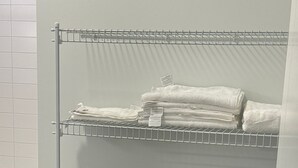 Een metalen draadrek met opgevouwen witte handdoeken en een zwarte prullenbak.
