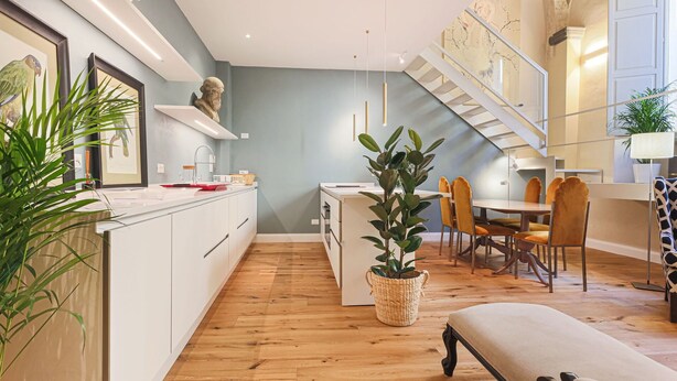 Una cucina moderna con mobili bianchi, un'isola centrale e un'area pranzo con una scala.