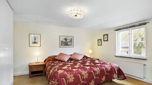 A bedroom with a floral bedspread, a bedside table with a lamp, and framed pictures on the wall. - Charming Townhouse in Central Ystad (Ystad)
