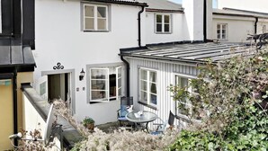 A white building with a black roof, a small patio with a table and chairs, and a window with a white frame. - Charming Townhouse in Central Ystad (Ystad)