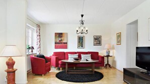 A living room with a red sofa, a coffee table, a chandelier, and a TV. - Charming Townhouse in Central Ystad (Ystad)