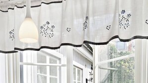 A room with a round table, a bowl of fruit, and a view through a window with a white curtain. - Charming Townhouse in Central Ystad (Ystad)