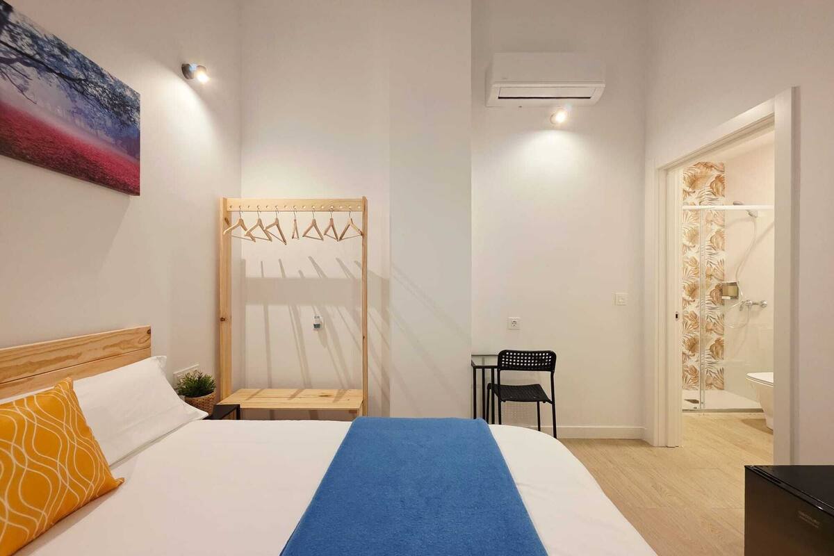 Een slaapkamer met een bed, een bureau, een stoel, een kledingkast en een airconditioning.