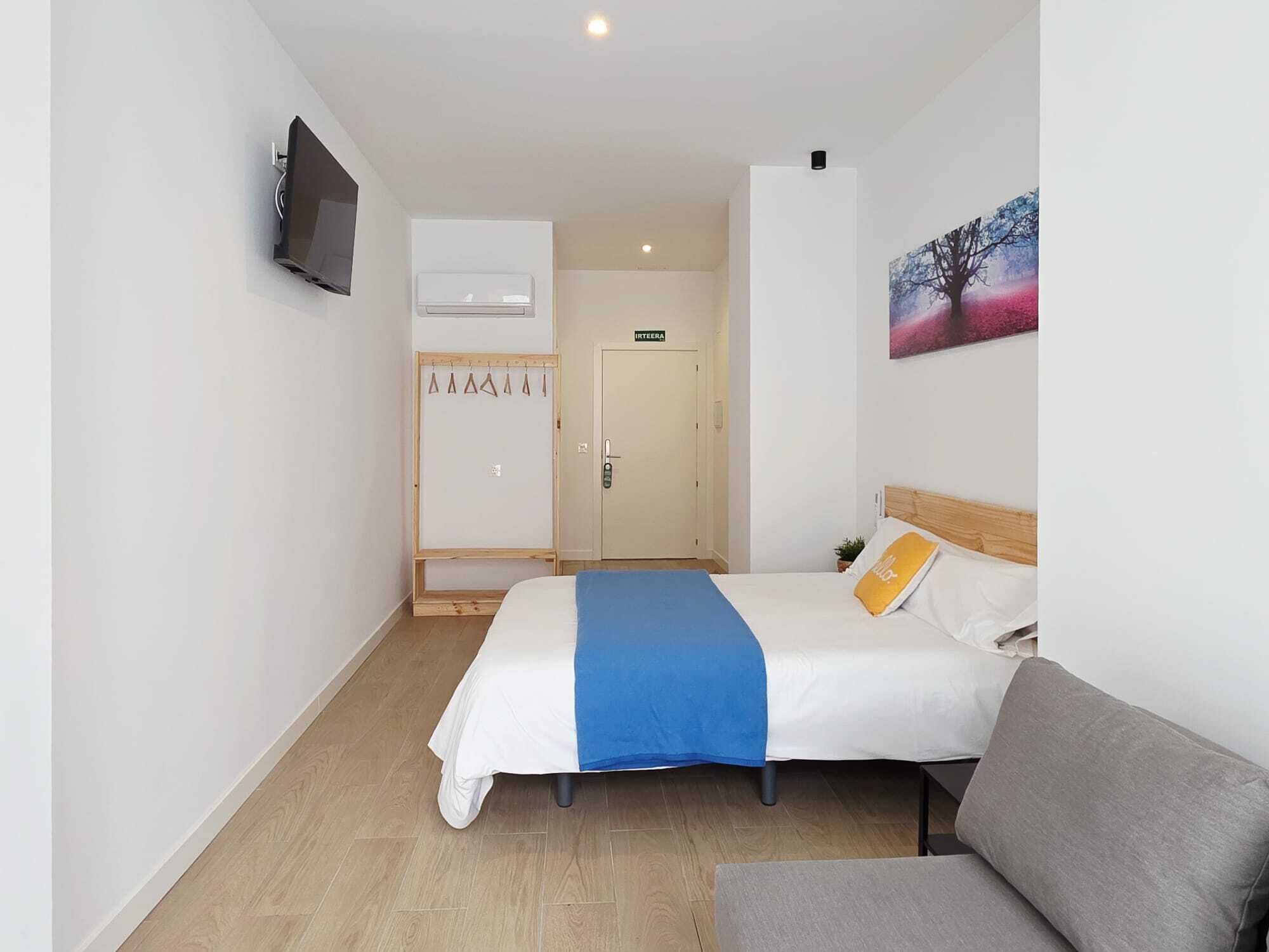 Una camera d'albergo con un letto, una TV, un appendiabiti e una porta.