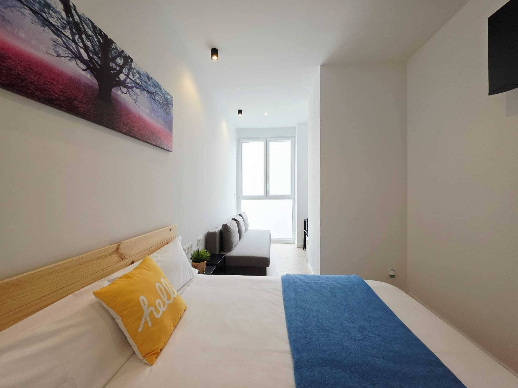 Una habitación de hotel moderna con cama, sofá, un cuadro y un ventanal grande.