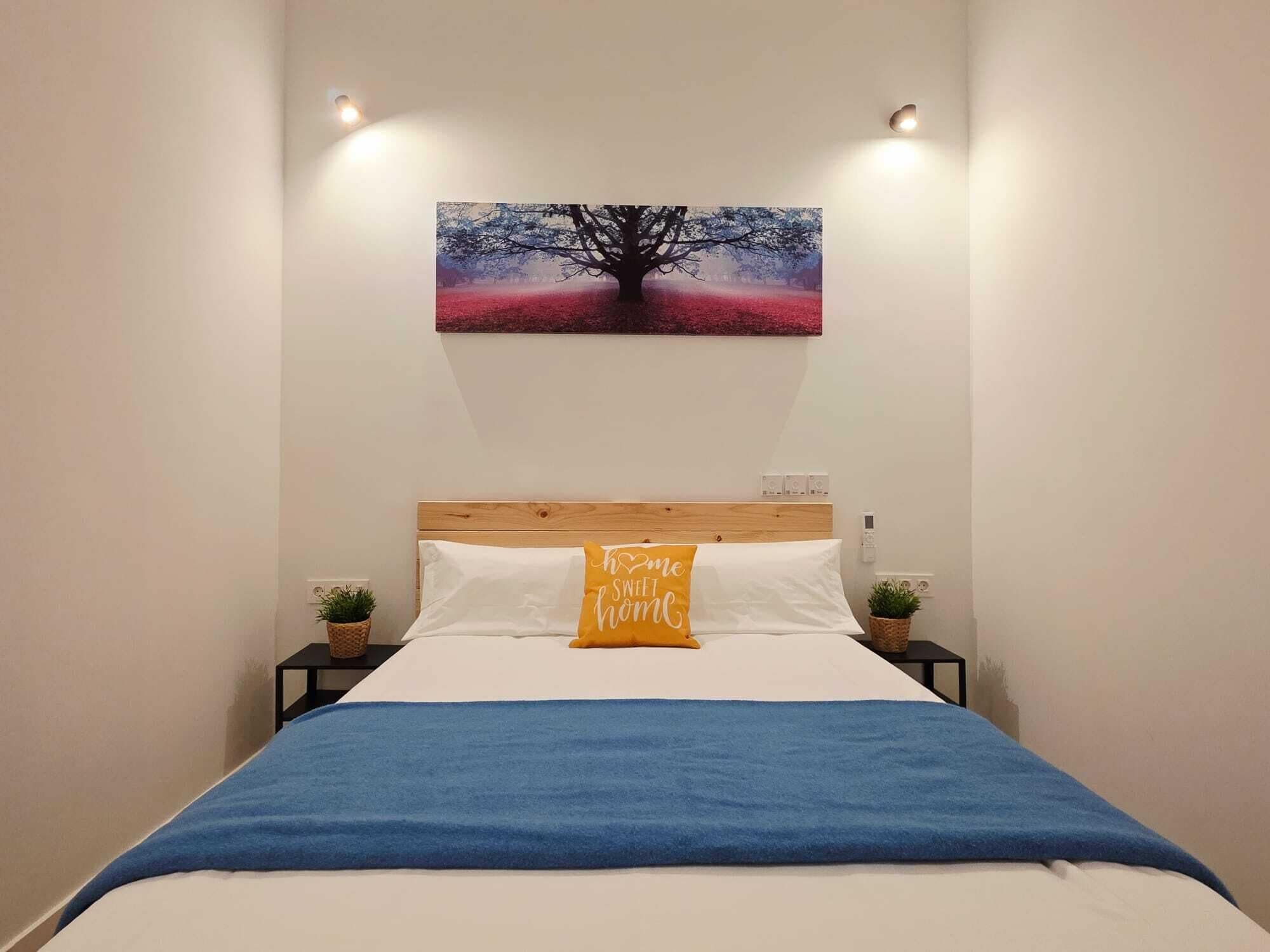 A bedroom with a bed, a wall-mounted painting, bedside tables, and a bedside plant.