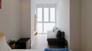 A bedroom with a bed, a bench, a small table, a plant, and a window with a view.