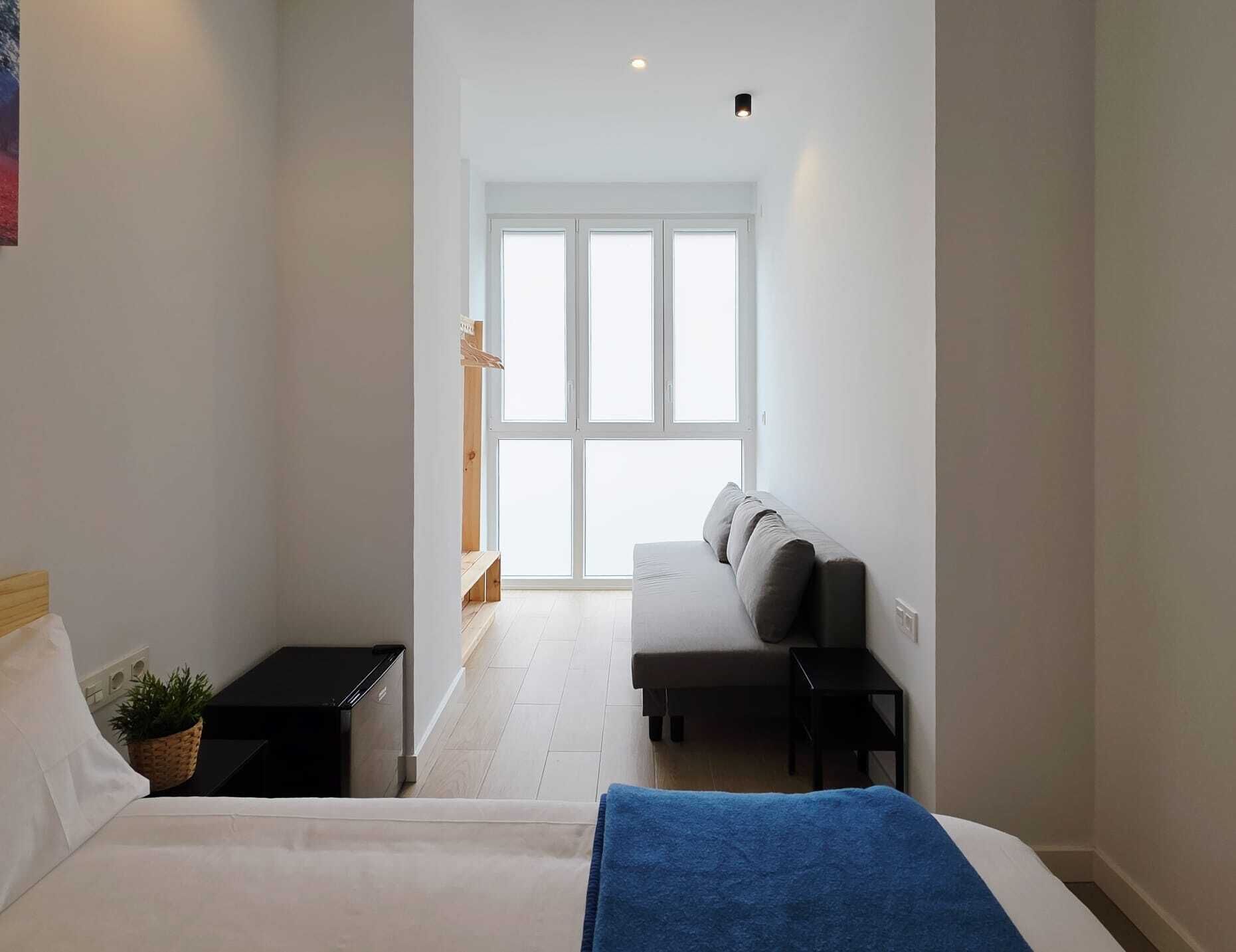 Ein Schlafzimmer mit Bett, einer Bank, einem kleinen Tisch, einer Pflanze und einem Fenster mit Blick.