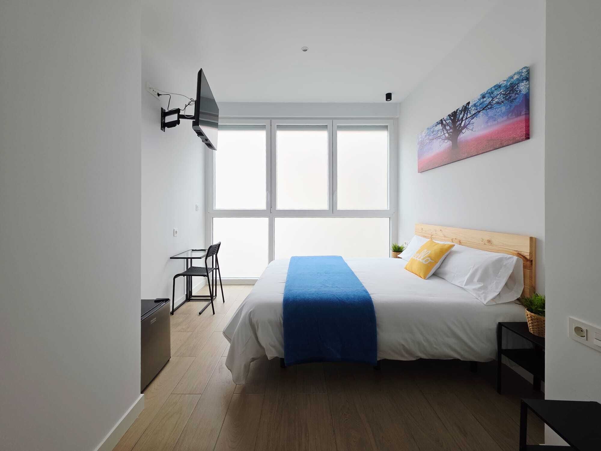 Un dormitorio moderno con una cama, un escritorio y un ventanal grande.