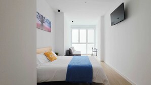 A hotel room with a bed, a TV mounted on the wall, a window, and a view of the outside.