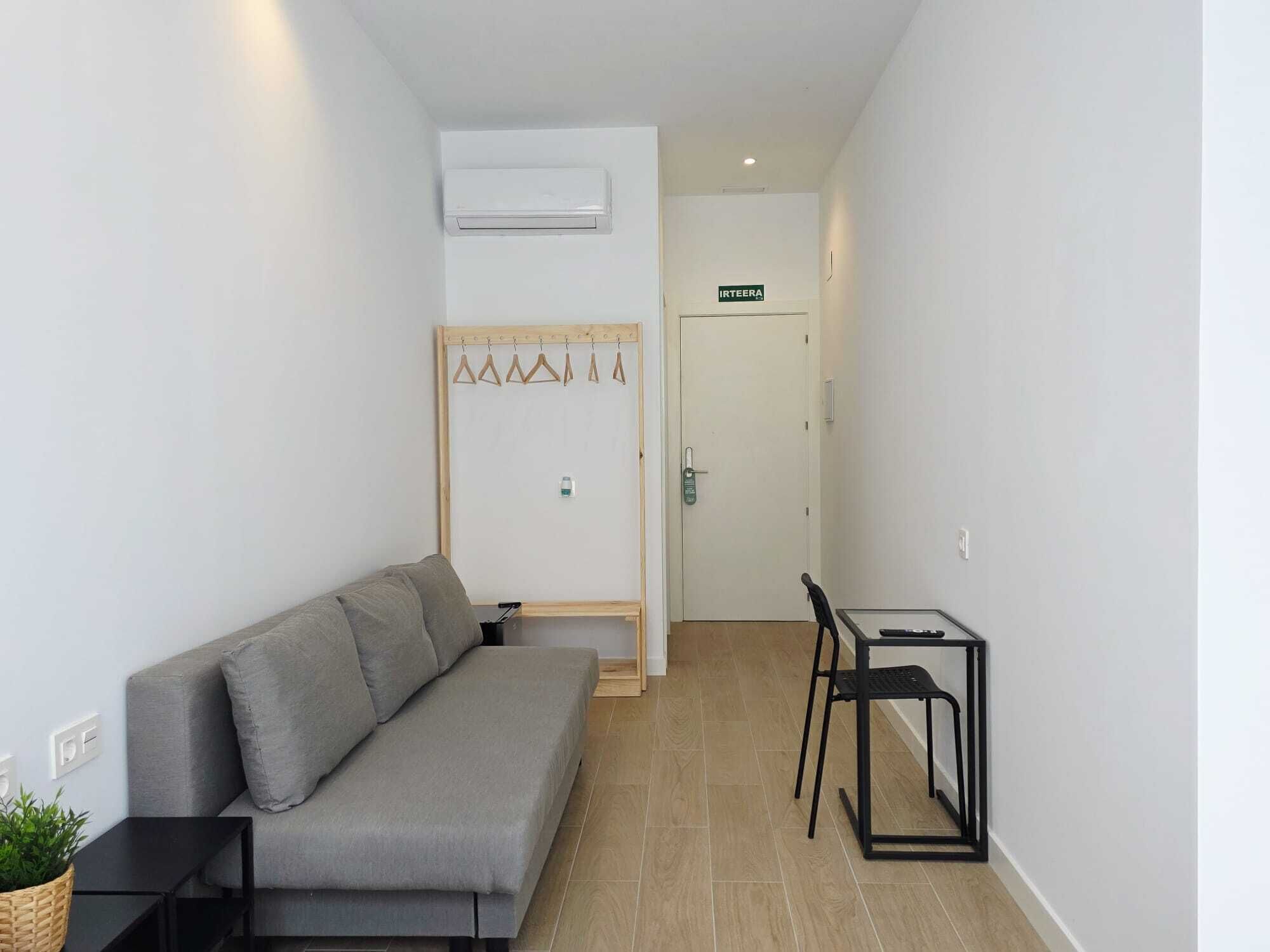 Een moderne kamer met een grijze bank, een klein tafeltje, een stoel en een kapstok met ophangers.